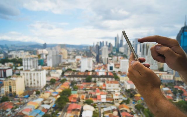 A man holding a smartphone on a street in Kuala Lumpur, Malaysia (Light Reading)