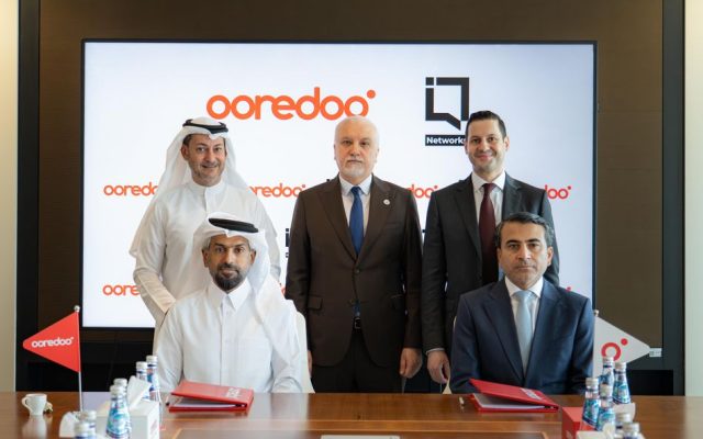 Five people seated at a table for a dark fibre agreement signing, with Ooredoo branding on a screen behind them