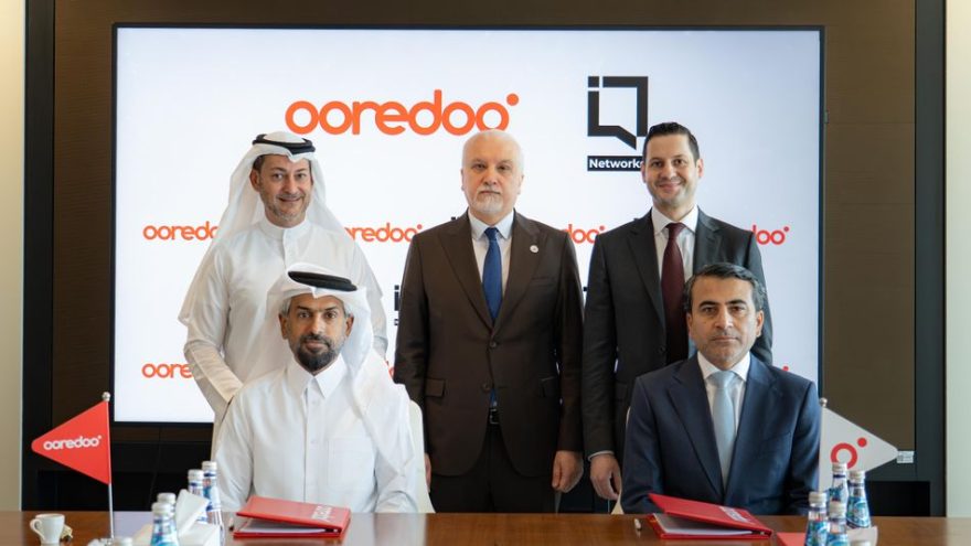 Five people seated at a table for a dark fibre agreement signing, with Ooredoo branding on a screen behind them
