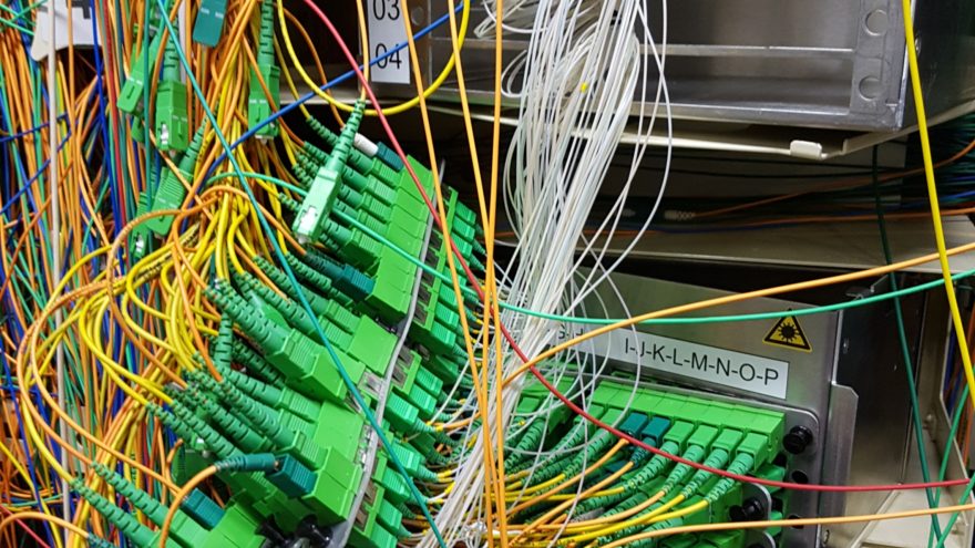 Labelled fibre optic patch panels with tangled patch cords inside a telecom equipment room